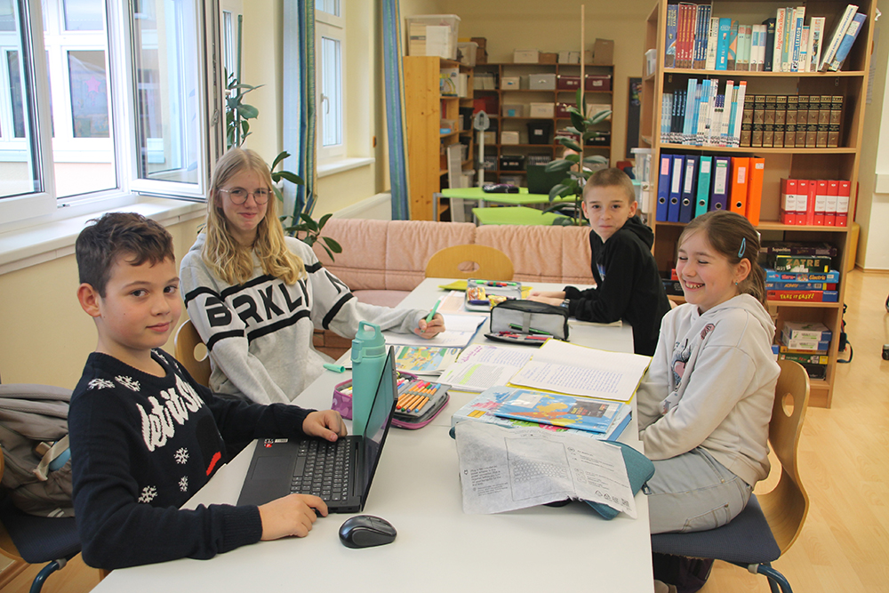 Das Bild zeigt Kinder die in der Bibliothek an einem Tisch zusammensitzen und lernen bzw. etwas gemeinsam spielen
