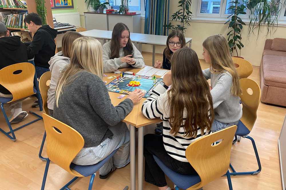 Das Bild zeigt Kinder die in der Bibliothek an einem Tisch zusammensitzen und etwas gemeinsam spielen