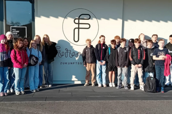 eine große Schülergruppe steht vor einem Schild mit einem Logo darauf