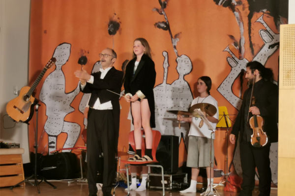 Auf dem Bild zu sehen ist eine Gruppe Kinder mit Lehrer, die singt und musiziert.