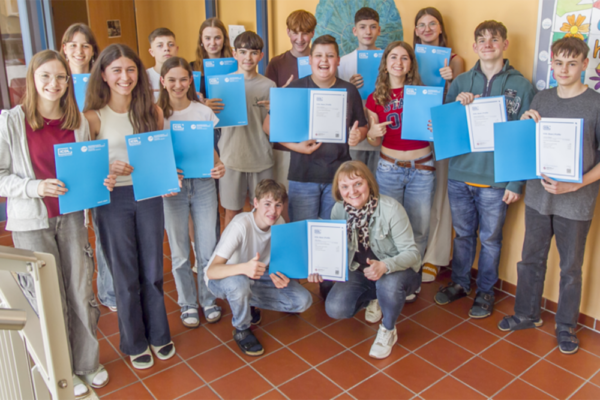 eine Gruppe Schüler lächelt stolz in die Kamera und hält ihre bestandenen Prüfungen in der Hand