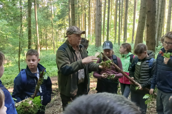 ein älterer Mann erklärt einer Gruppe von Schülern etwas über den Wald